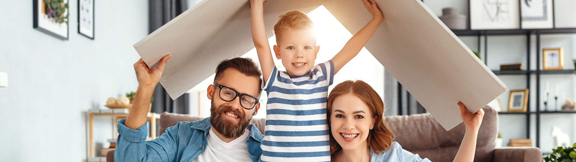 Eine Familie ist zuhause und hält sich ein Stück Holz über den Kopf. Das Holz hat die Form eines Dachs.