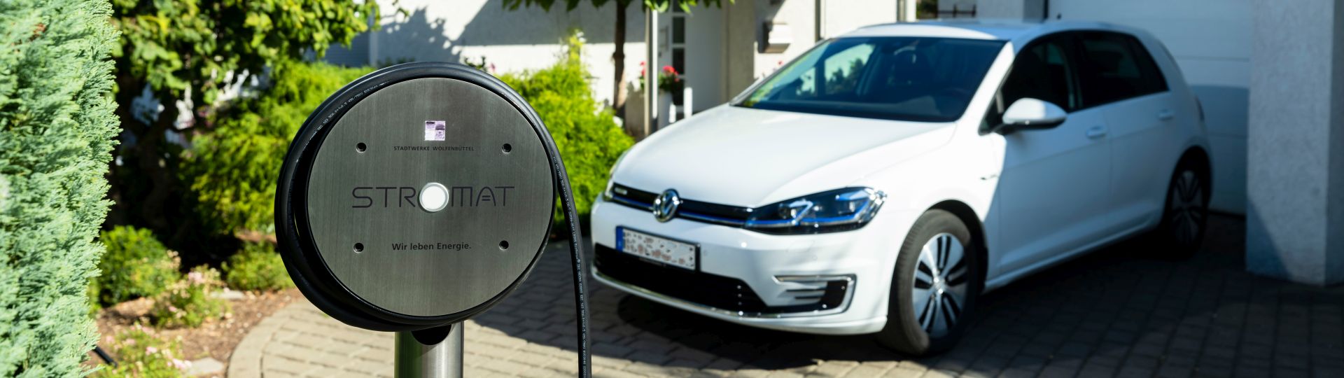 Die Wallbox Stromat der Stadtwerke Wolfenbüttel steht vor einem Haus mit Elektroauto.