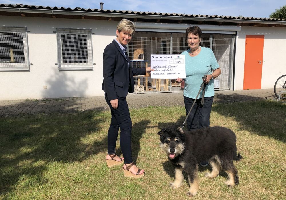 Zwei Frauen mit einem Spendencheck und einem Hund 